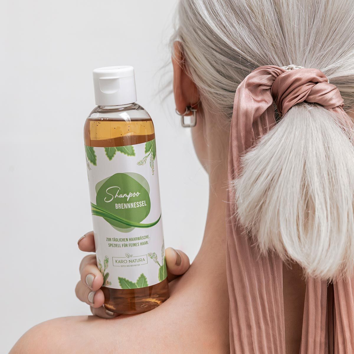Person hält Shampoo-Flasche. Person mit blonden Haaren und rosa Haargummi.