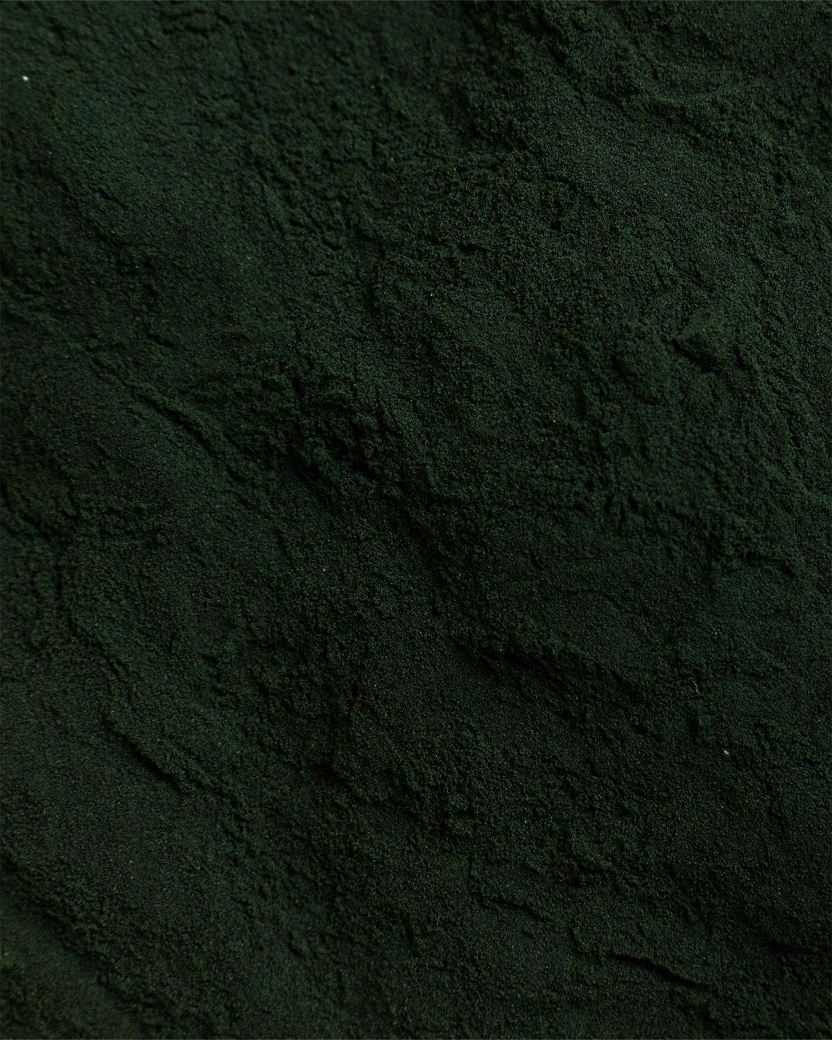 Nahaufnahme von dunkelgrünem Spirulina-Pulver. Die Textur ist körnig und unregelmäßig.