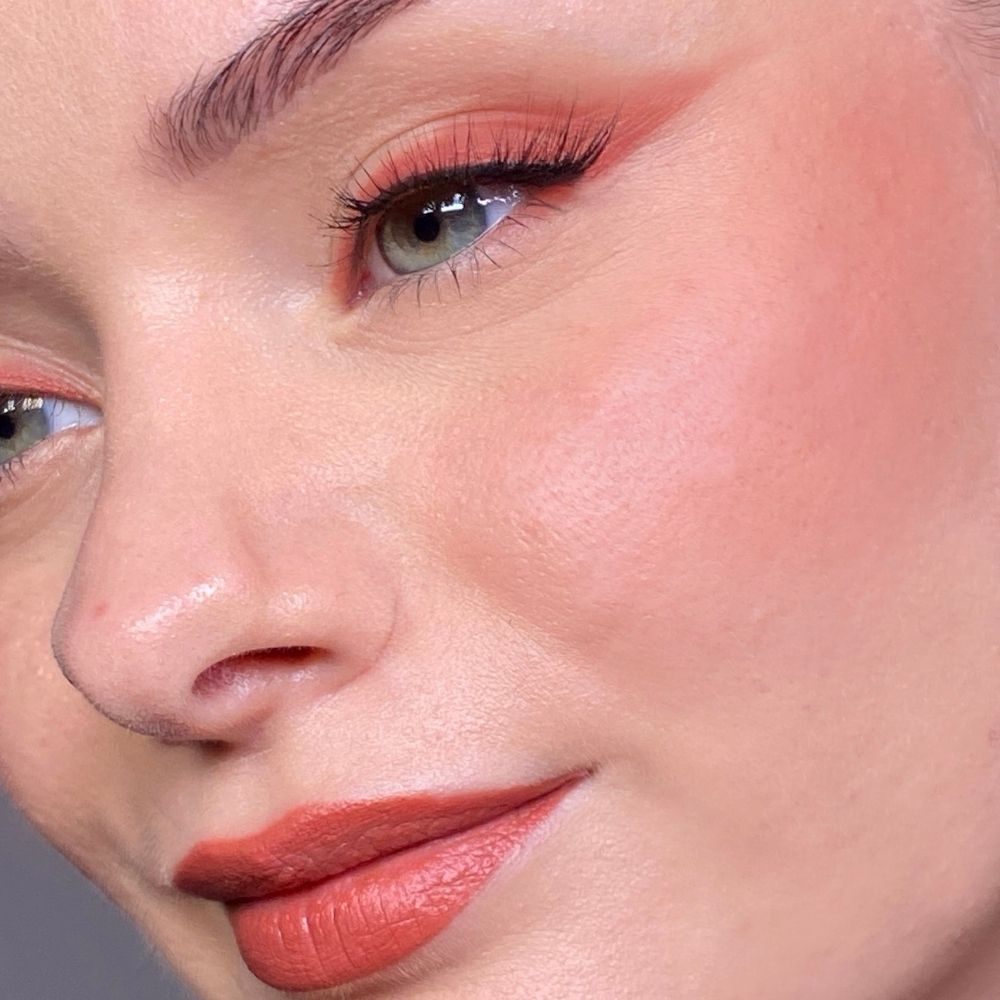 Nahaufnahme eines Gesichts mit geschminkten Augen, Wangen und Lippen. Lippenstift in Korallenrot. Hautton: hell.
