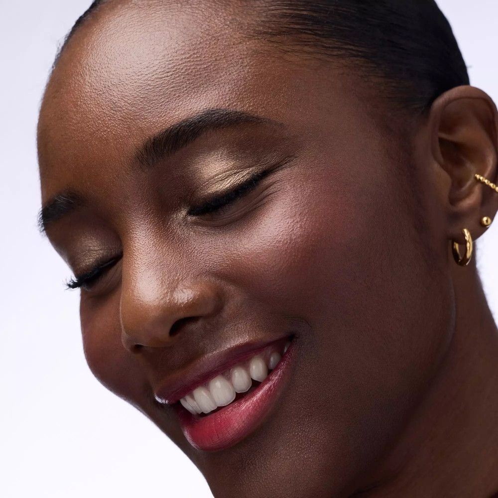 Nahaufnahme einer Frau mit goldfarbenem Lidschatten. Geschlossene Augen. Goldener Ohrschmuck.