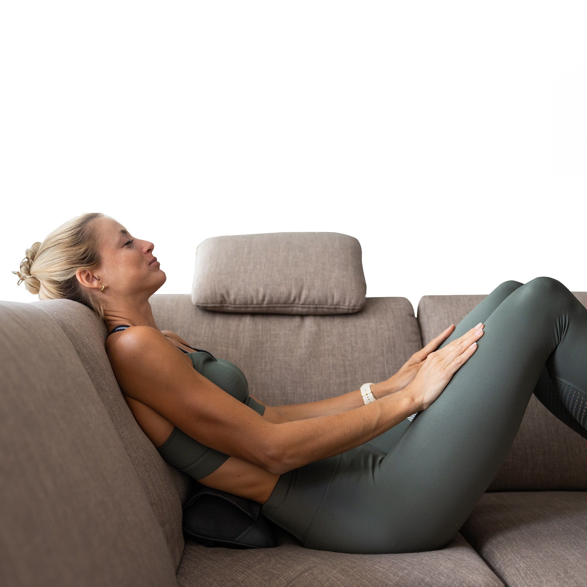 Frau auf Sofa mit Massagekissen am unteren Rücken. Schwarzes Kissen. Frau mit geschlossenen Augen.
