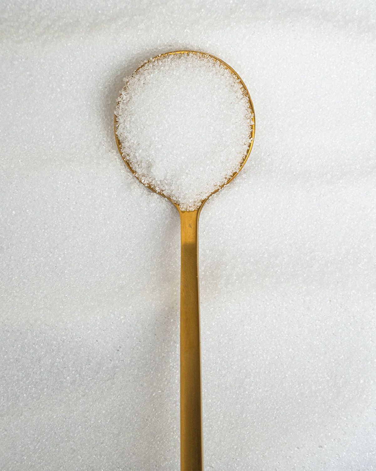 Ein goldener Löffel gefüllt mit Süßstoff, liegend auf einer Fläche aus Süßstoffkristallen.