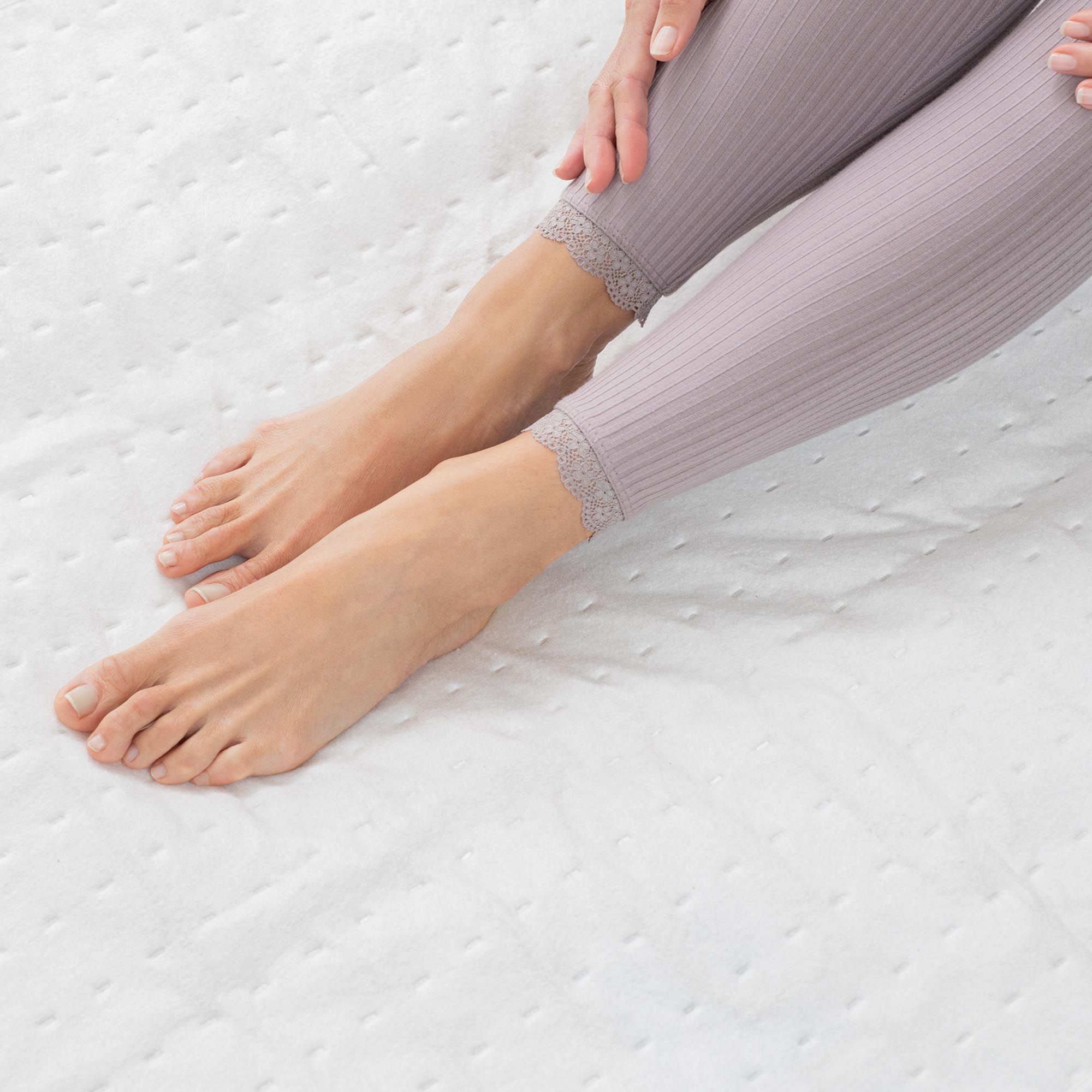 Nahaufnahme von Füßen auf einem weißen Wärmeunterbett. Person trägt Leggings.