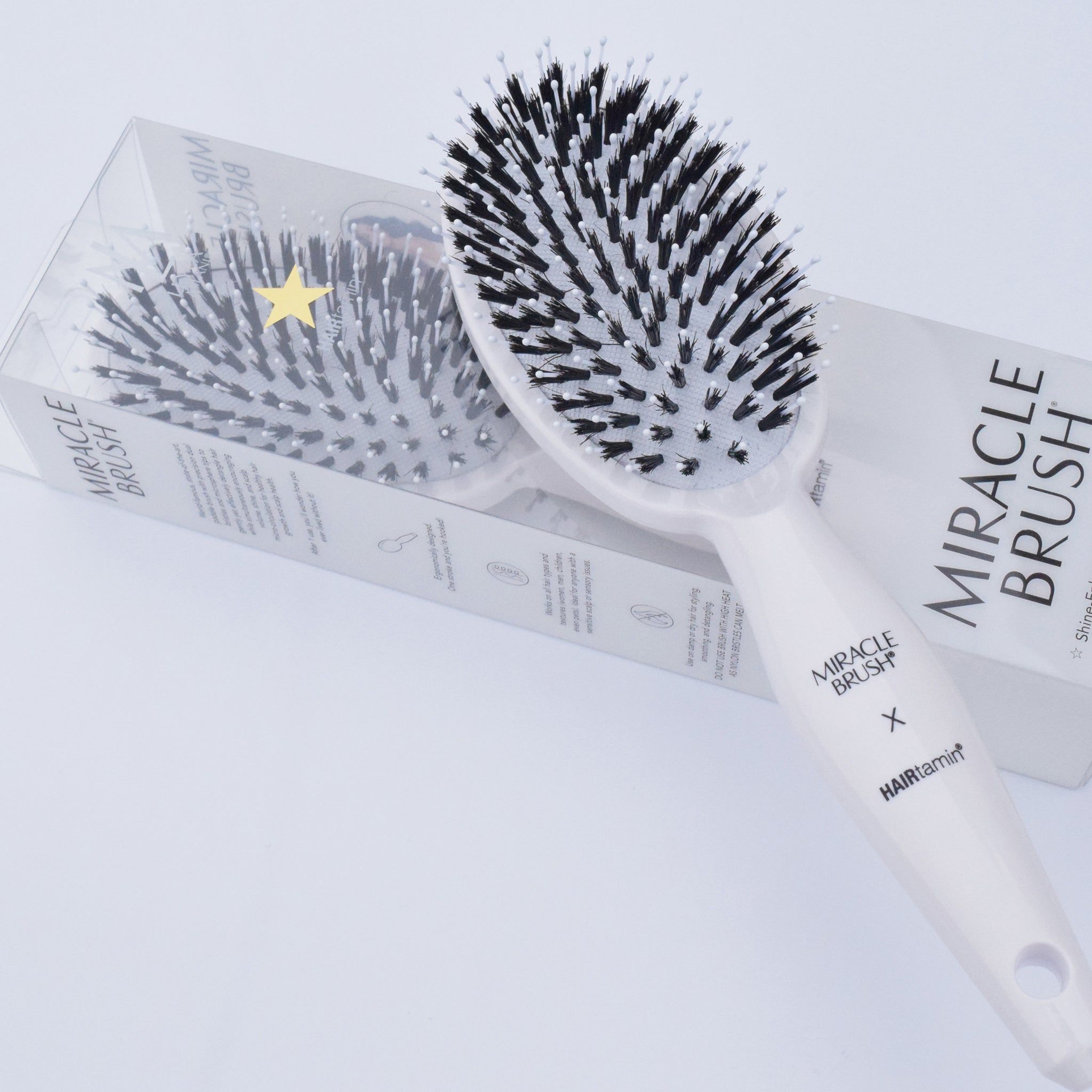 Weiße Bürste mit schwarzem Borsten in Verpackung. Aufschrift MIRACLE BRUSH X HAIRtamin.