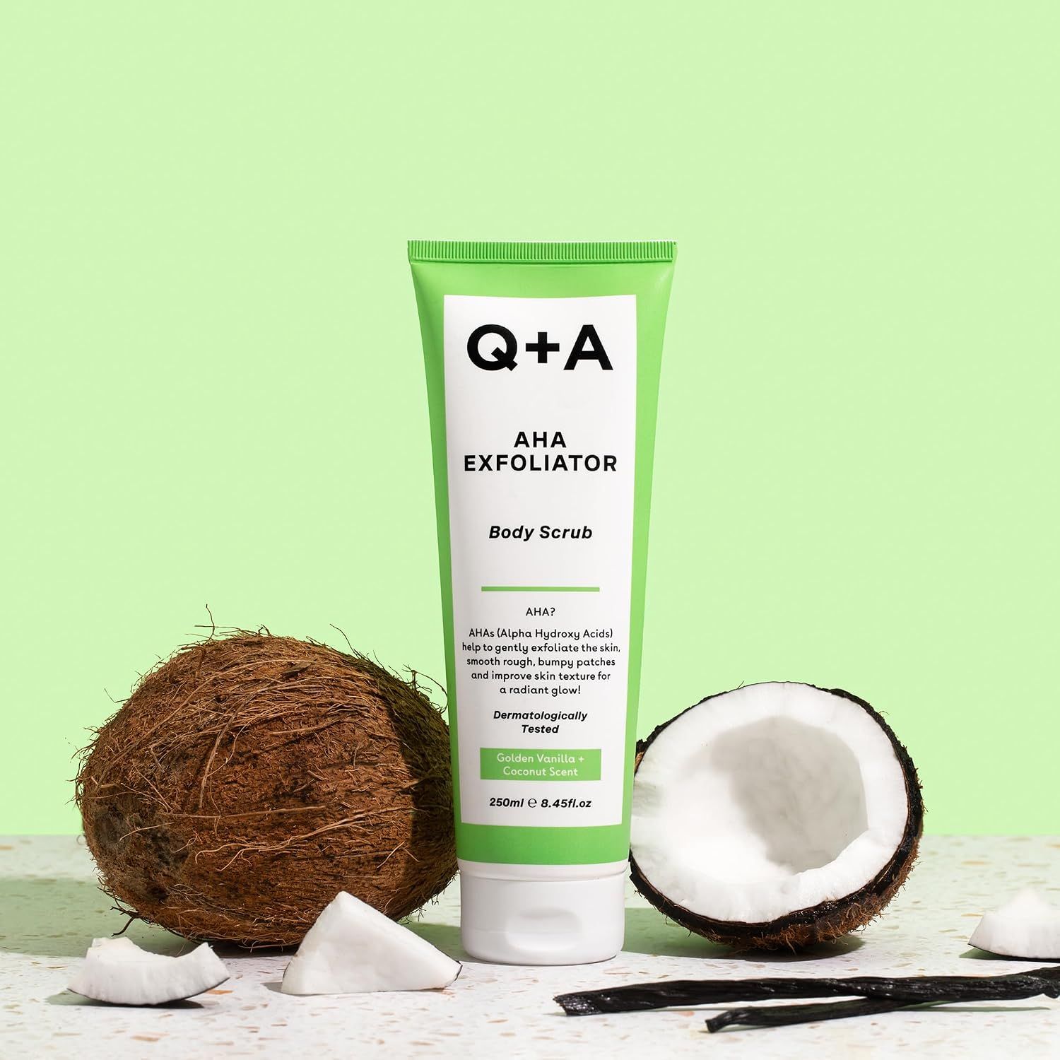 Q+A AHA Exfoliator Body Scrub in einer grünen Tube mit Kokosnuss.