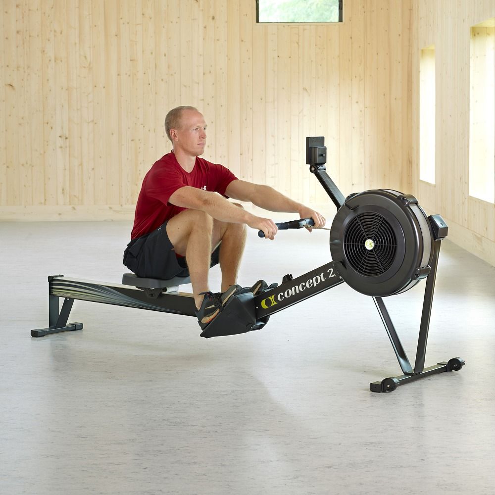 Ein Mann trainiert auf einem Concept2 RowErg. Das Gerät ist schwarz. Der Hintergrund ist hell und holzgetäfelt.