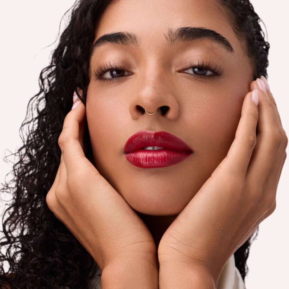 Porträt einer Frau mit Lippenstift. Dunkelroter Lippenstift. Hände umrahmen das Gesicht.