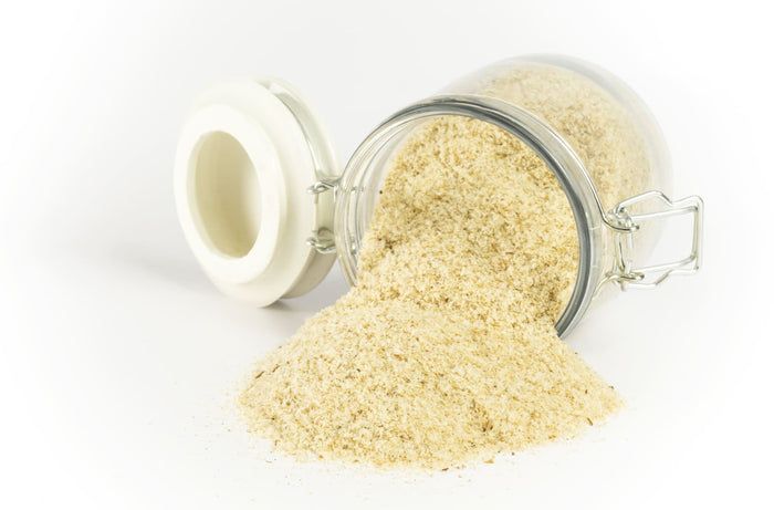 Glasbehälter mit "buXtrade Bio Flohsamenschalen". Offenes Glas, Inhalt wird ausgeschüttet. Helles Pulver.