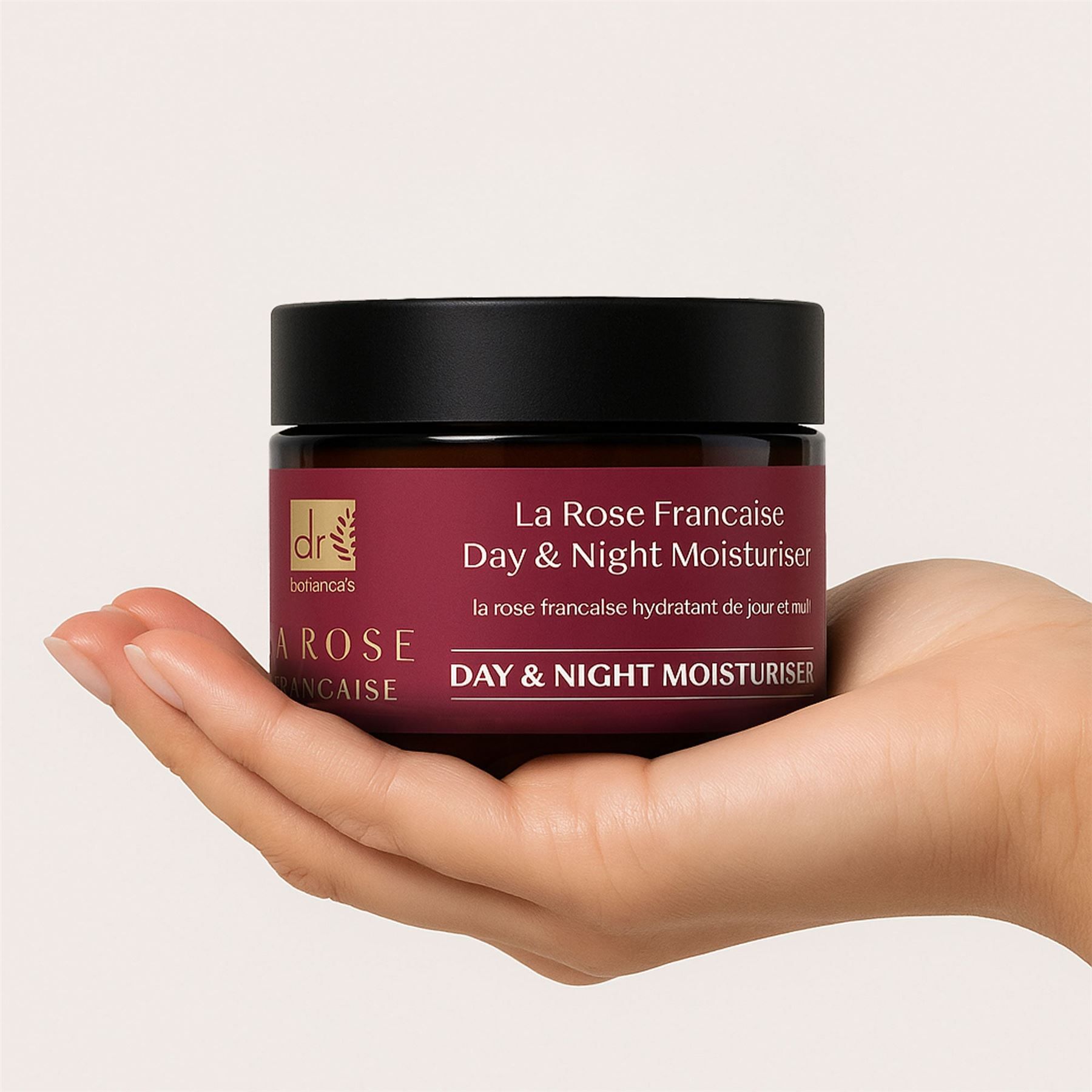 Eine Hand hält ein Glas Dr. Botanicals La Rose Française Tages- und Nachtcreme.