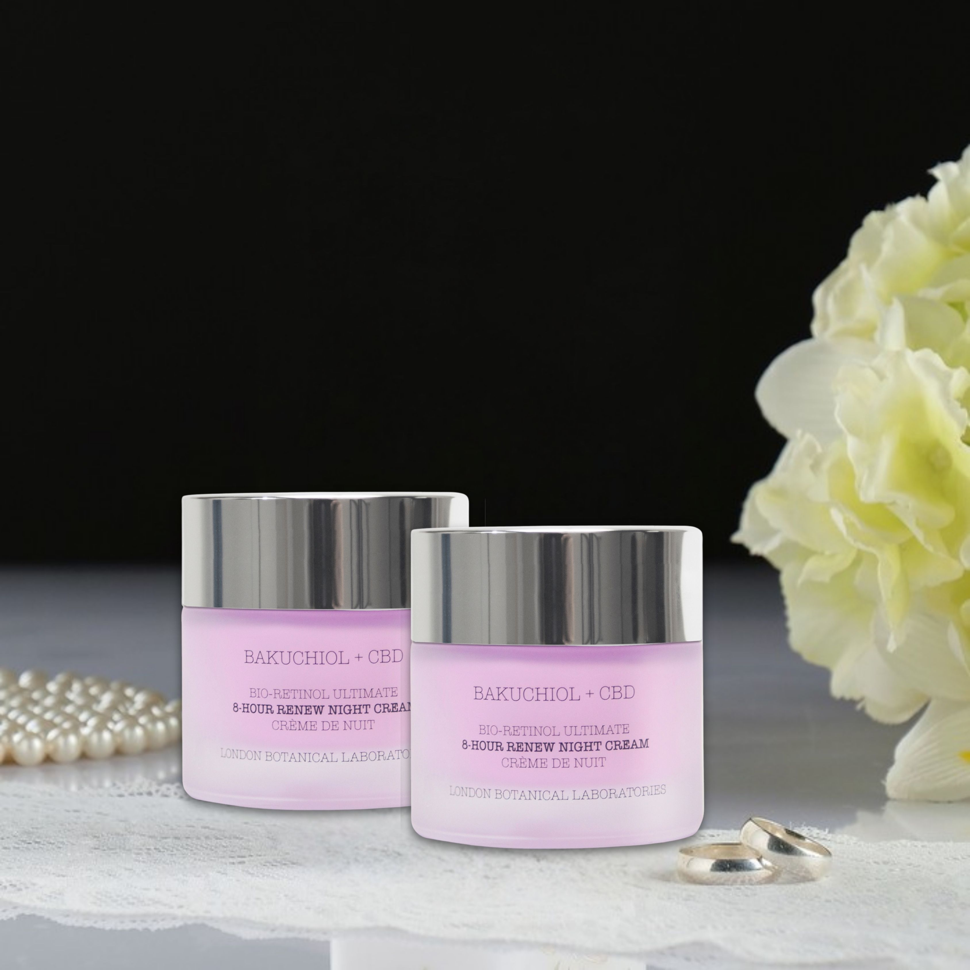 Zwei Tiegel Nachtcreme mit silbernen Deckeln. Aufschrift: Bakuchiol + CBD. Blüten und Schmuck im Hintergrund.