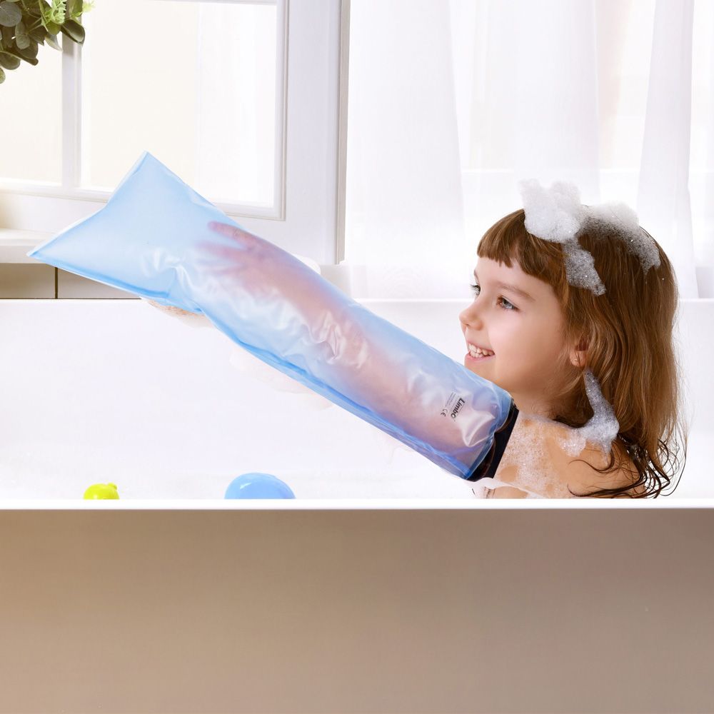 Ein Kind in einer Badewanne mit einem blauen Duschschutz für einen Gipsverband am Arm. Das Kind lächelt. Schaum um das Gesicht.