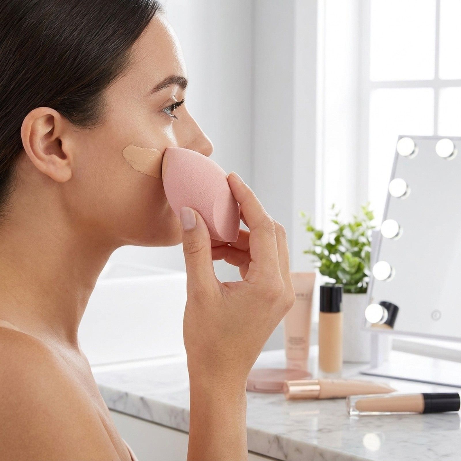 Eine Frau trägt flüssiges Make-up mit einem rosafarbenen Schwamm auf.