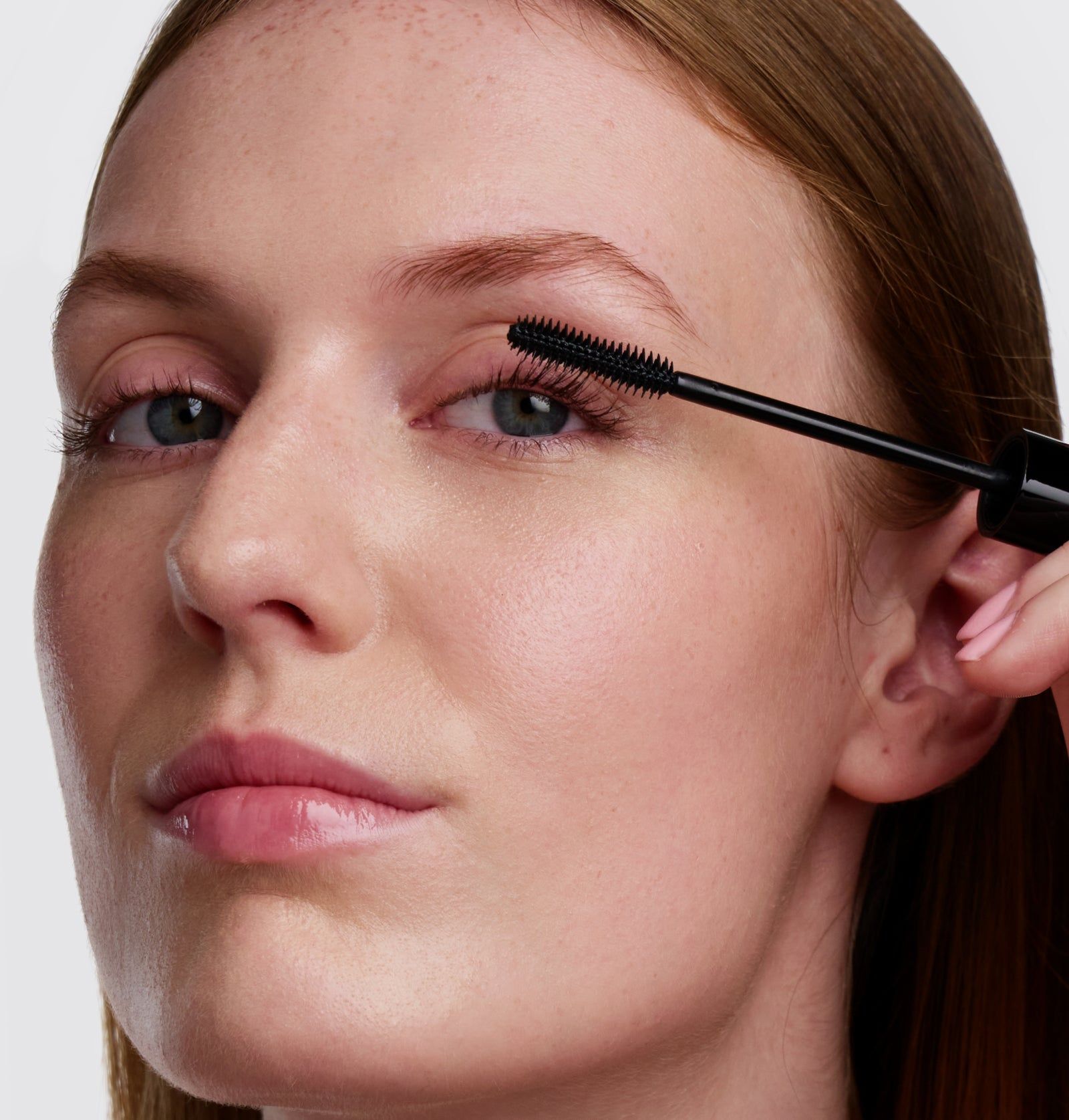 Eine Frau trägt Wimperntusche auf. Schwarze Mascara-Bürste in der Nähe des Auges. Helle Haut, rotes Haar.