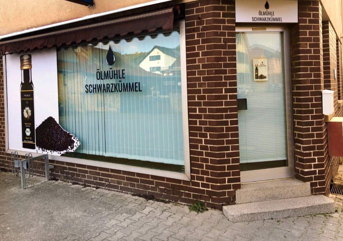 Geschäft mit dem Logo Ölmühle Schwarzkümmel. Auf dem Fenster ein Bild von Schwarzkümmel und Ölflasche. Ziegelmauer.