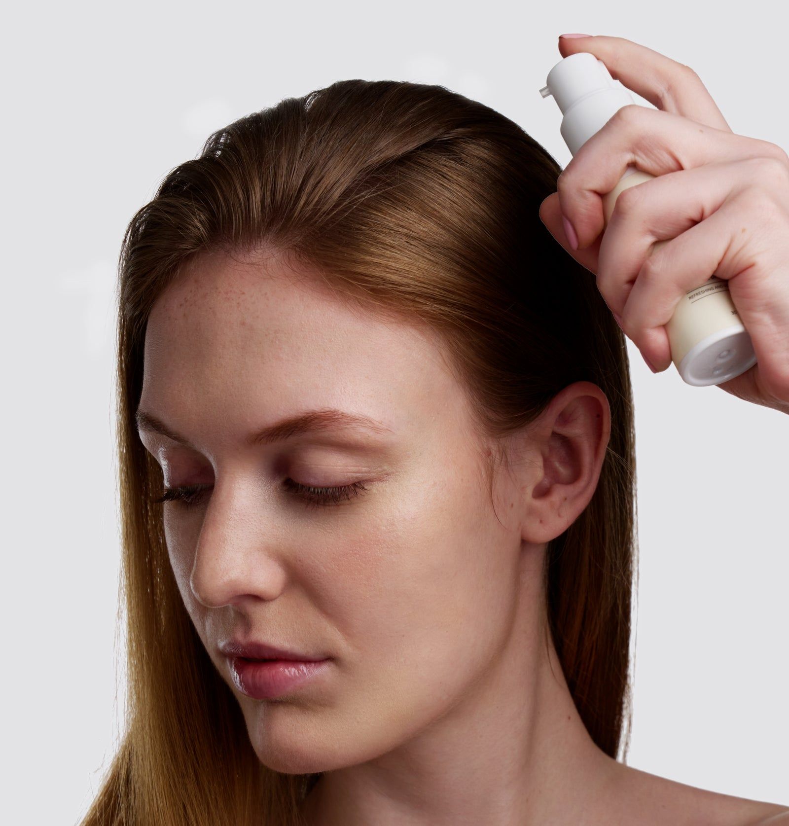 Person sprüht Trockenshampoo auf das Haar einer Frau. Die Frau hat lange, braune Haare.