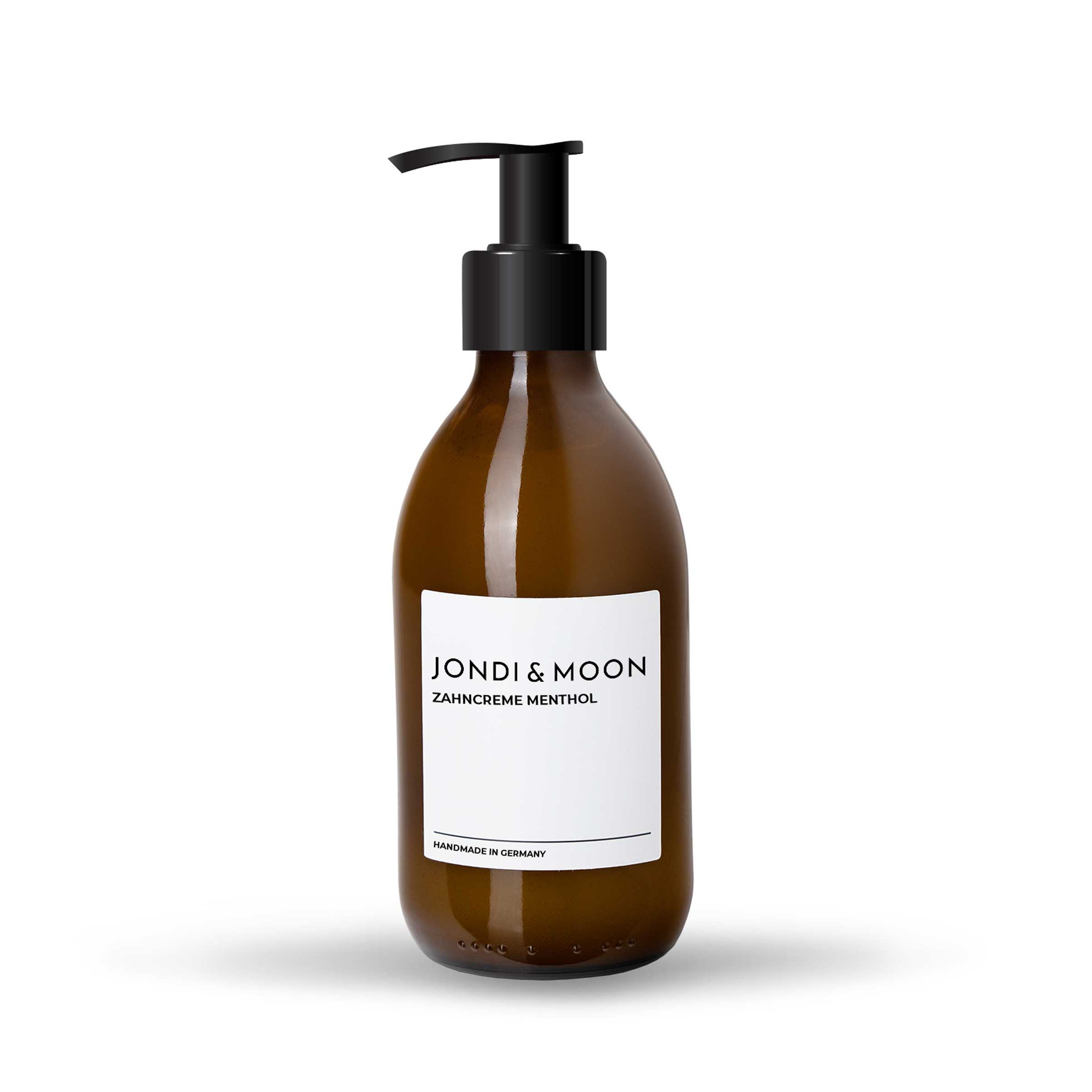 Braune Glasflasche mit schwarzem Pumpkopf. Weißes Etikett mit Schriftzug: JONDI & MOON, Zahncreme Menthol. "Handmade in Germany".