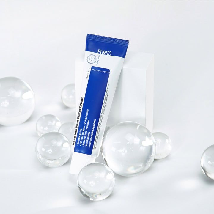 Eine Tube Deep Sea Pure Water Cream steht auf einer weißen Oberfläche, umgeben von Glaskugeln. Die Tube ist weiß und blau.