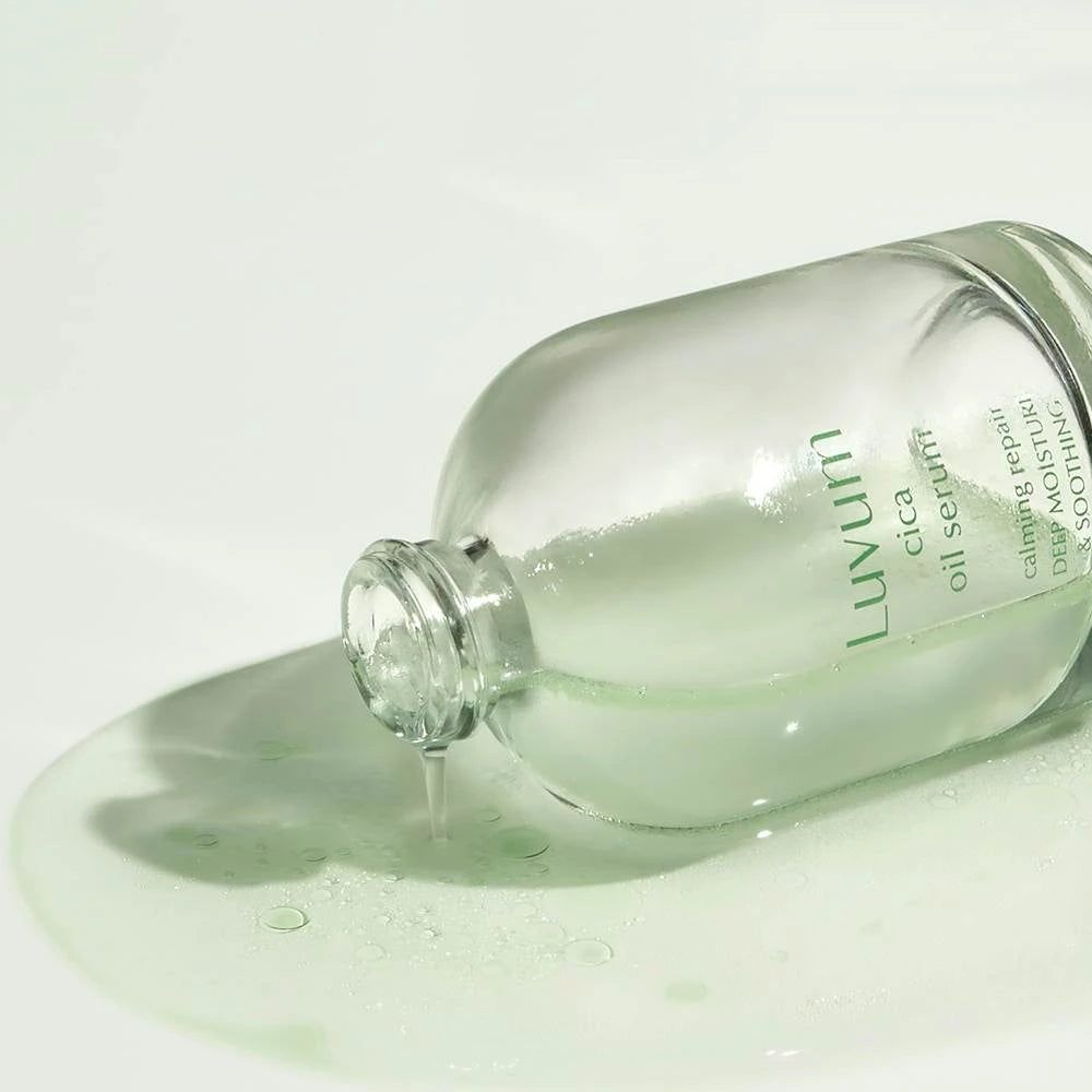 Serumflasche liegt auf einer Oberfläche. Serum fließt aus der Flasche. Aufschrift: Luvum cica oil serum. Text: real calming repair, deep moisture & soothing.