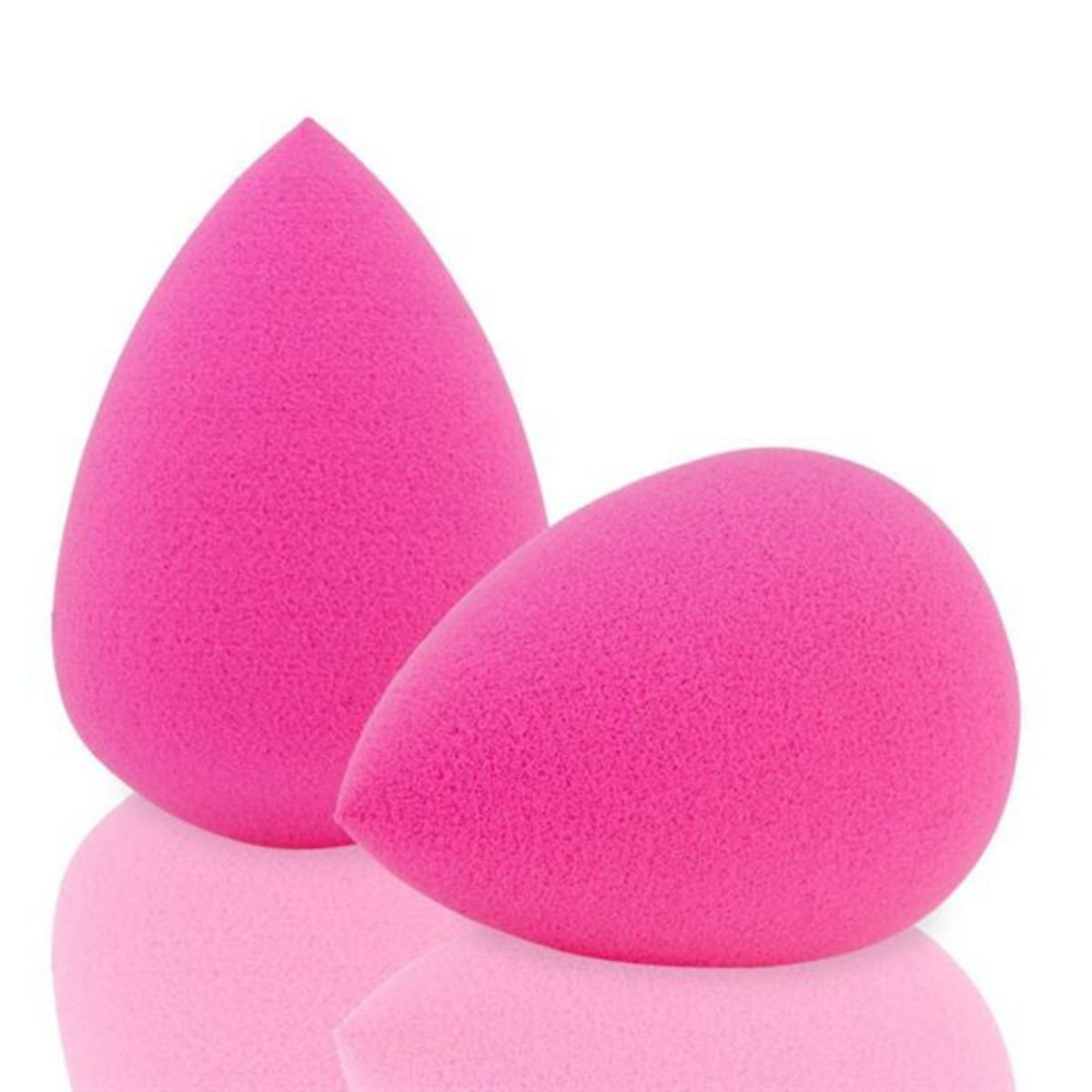 Zwei leuchtend pinke Make-up-Schwämme in Tropfenform, auf einer reflektierenden Oberfläche.