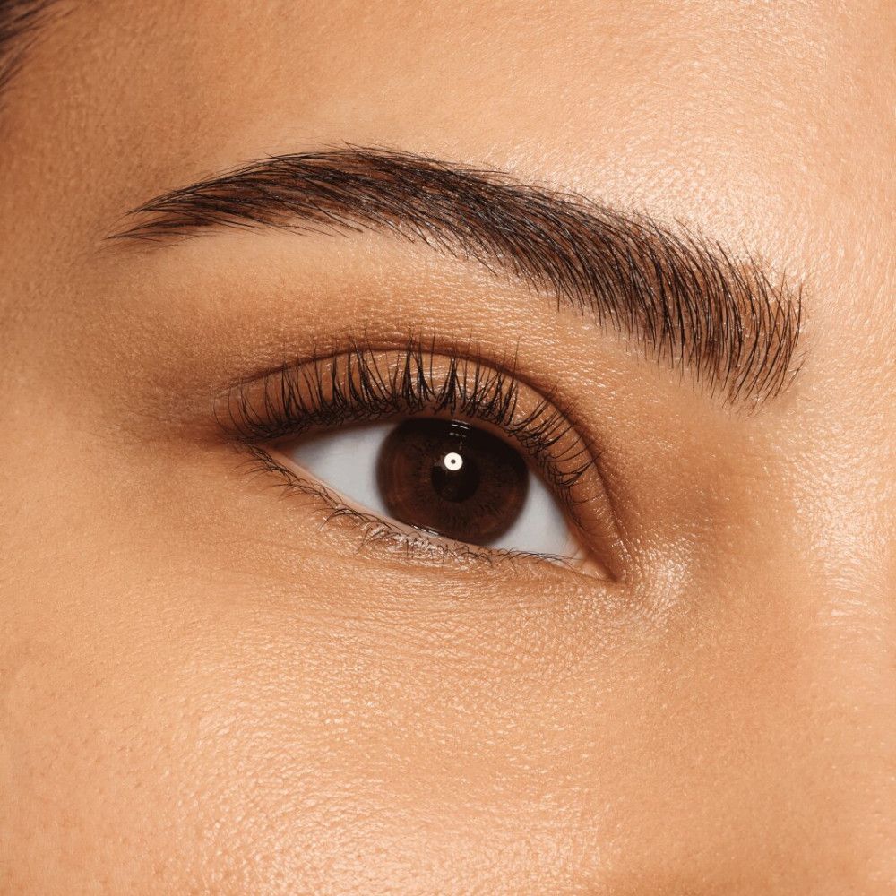 Nahaufnahme eines Auges mit geformten Augenbrauen. Das Auge ist braun und die Wimpern sind getuscht.