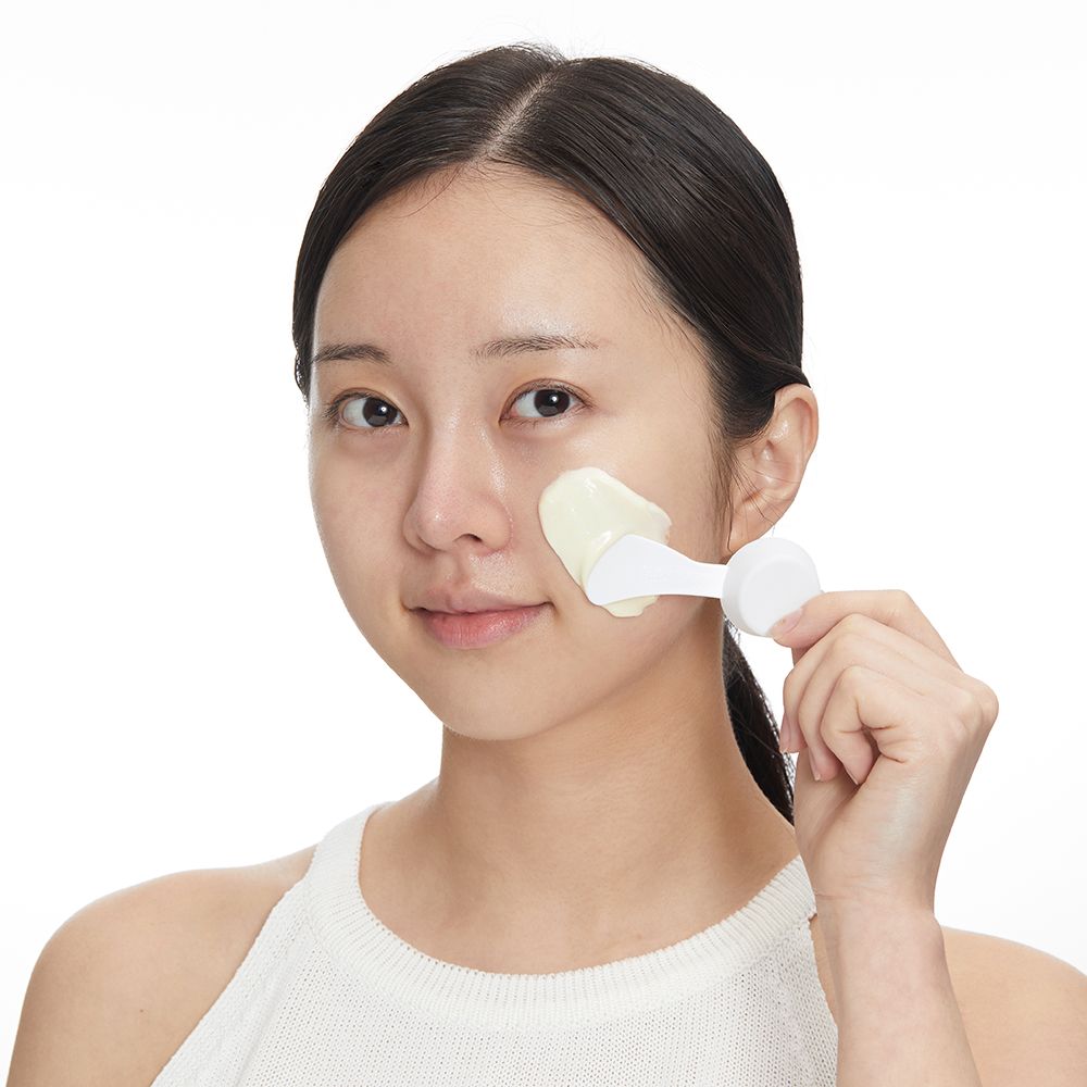 Frau trägt Modeling Pack Maske mit einem Spatel auf ihr Gesicht auf.