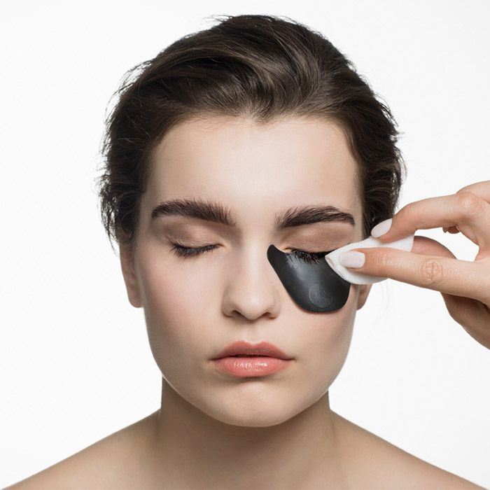 Gesicht einer Frau mit Augenpads. Eine Hand entfernt ein Augenpad mit einem Wattepad.
