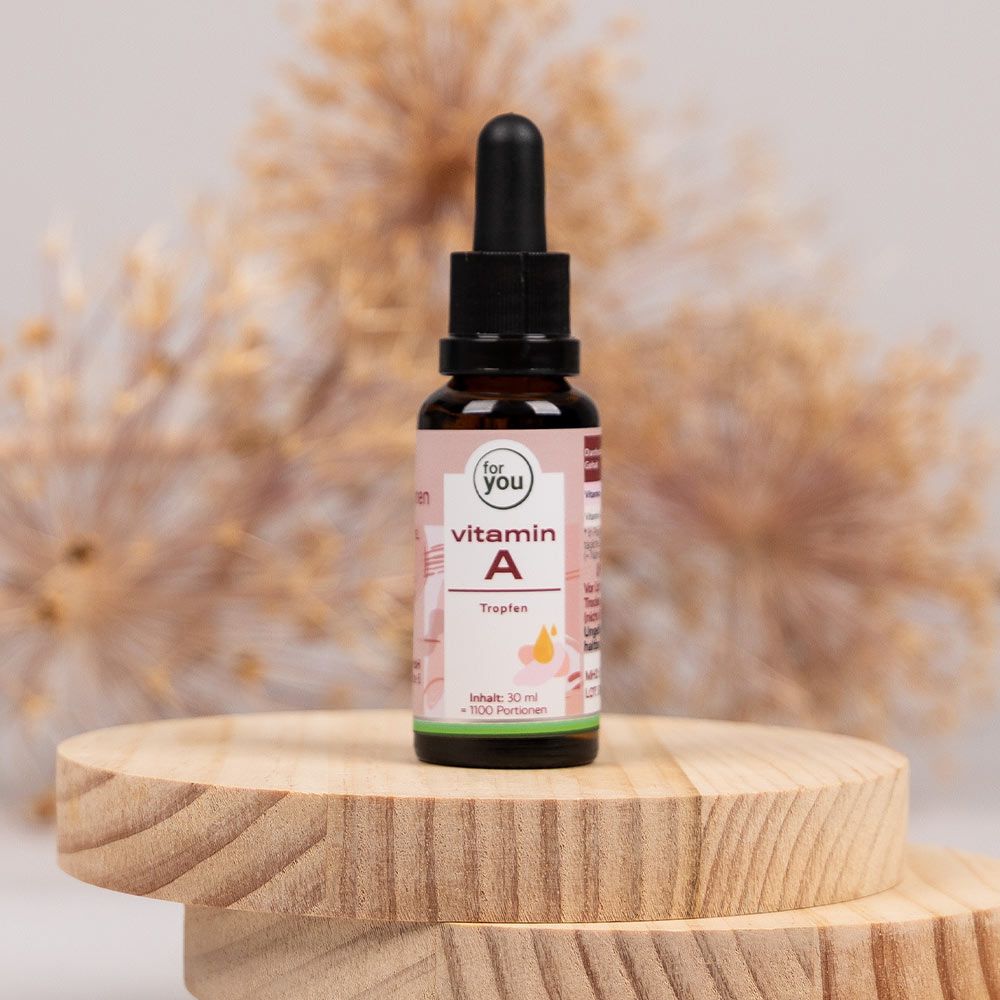 Braune Glasflasche mit Tropfer auf Holzsockel. Aufschrift: for you Vitamin A Tropfen. Rosa Etikett mit gelben Tropfen.