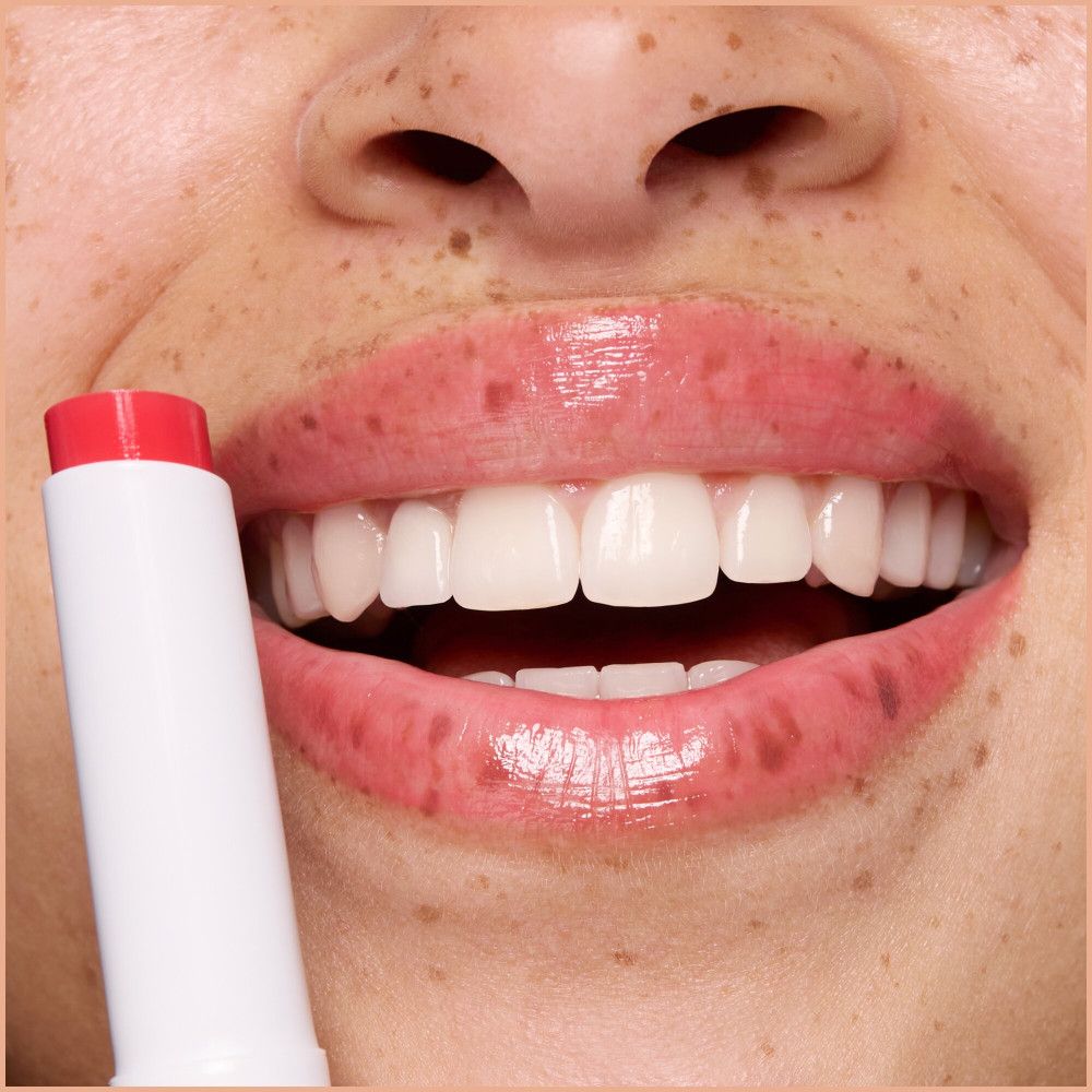 Nahaufnahme von Lippen mit Lippenbalsam. Ein weißer Lippenbalsam-Stift wird gehalten.