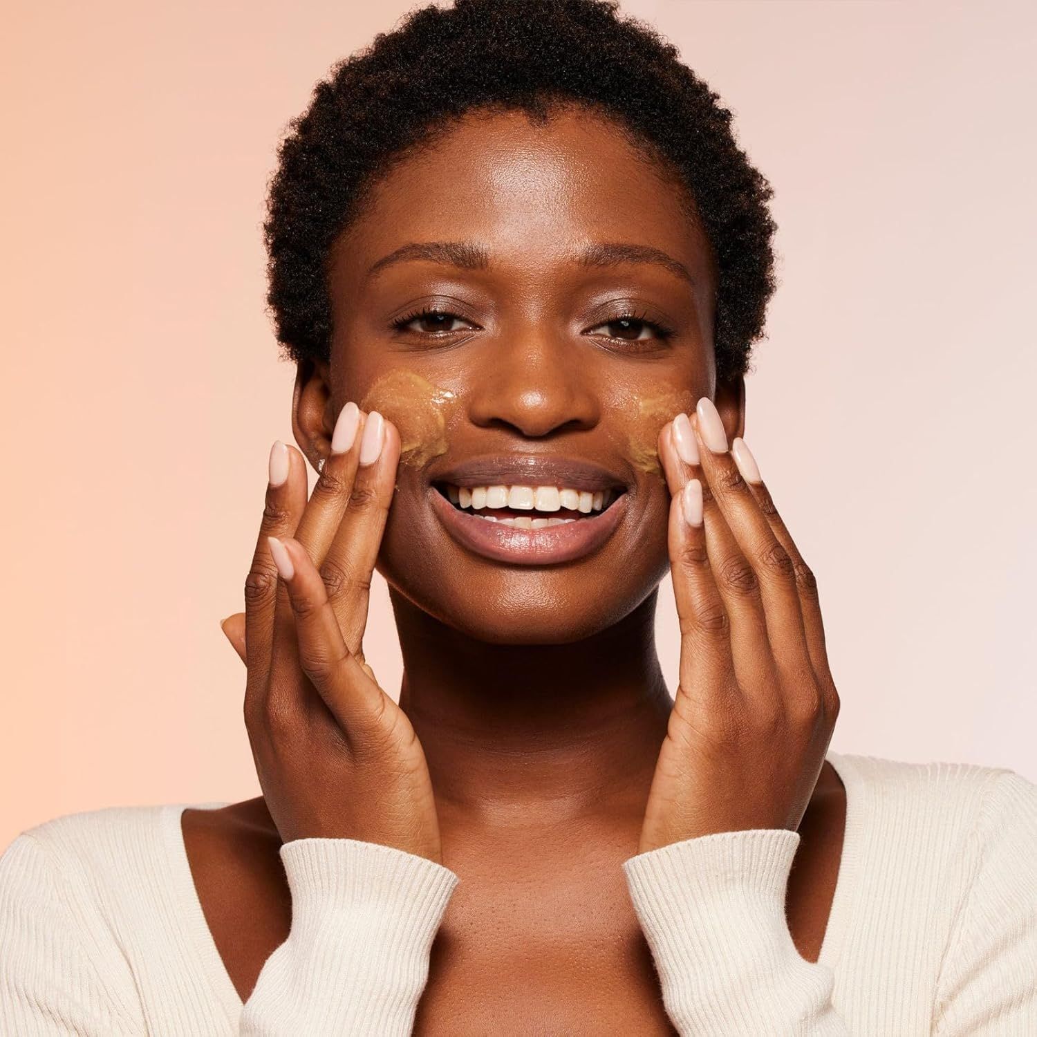 Frau mit Produkt auf Gesicht aufgetragen. Hände berühren sanft die Haut. Gelbliche Substanz sichtbar.