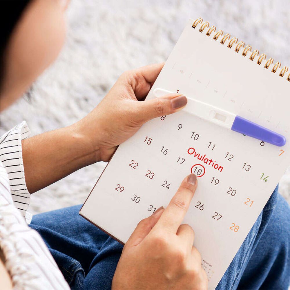 Person mit Ovulationstest und Kalender. Der 18. Tag ist markiert. Der Test liegt auf dem Kalender.