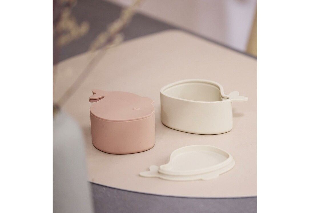 Zwei walförmige Brotdosen, eine geöffnet, eine mit Deckel. Farben: Rosa und Beige. Deckel liegen daneben.