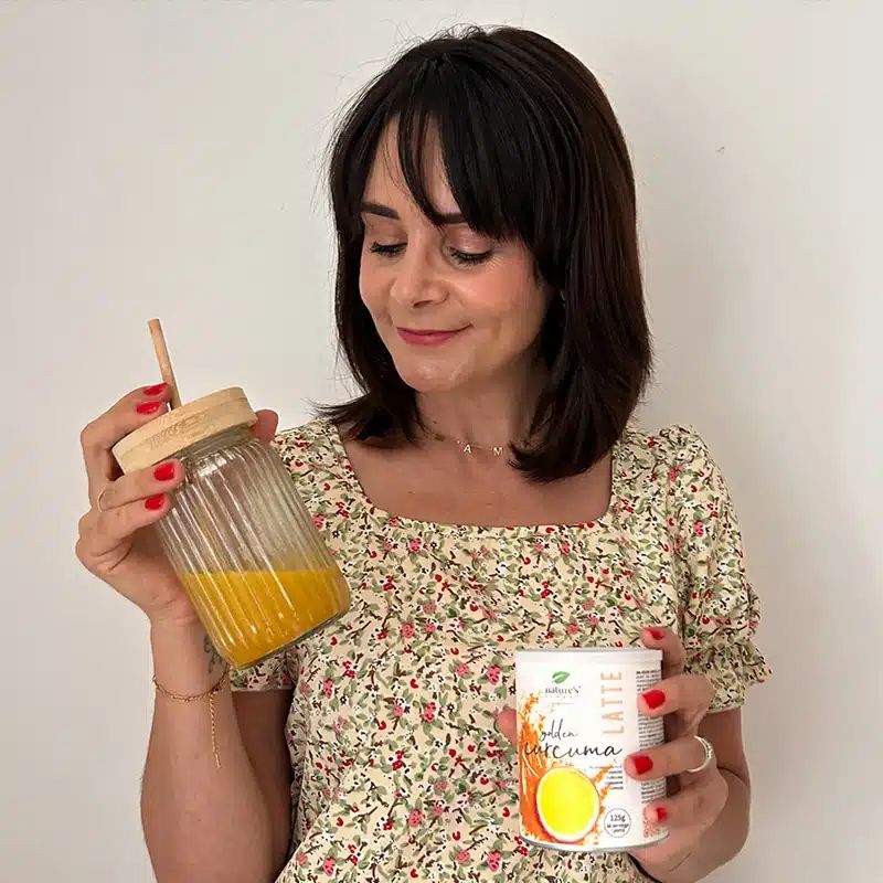 Frau hält ein Glas mit goldenem Getränk und eine Dose Nature's Finest Golden Curcuma Latte.