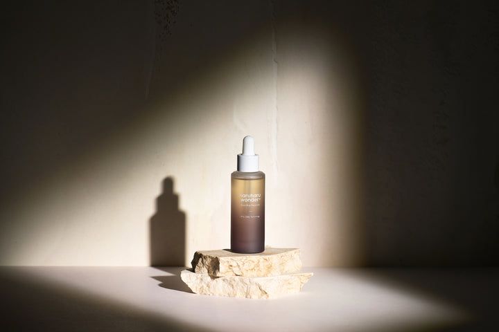 HaruHaru Wonder Black Rice Facial Oil Flasche auf Stein. Braune Flasche mit weißem Deckel, im Schatten.