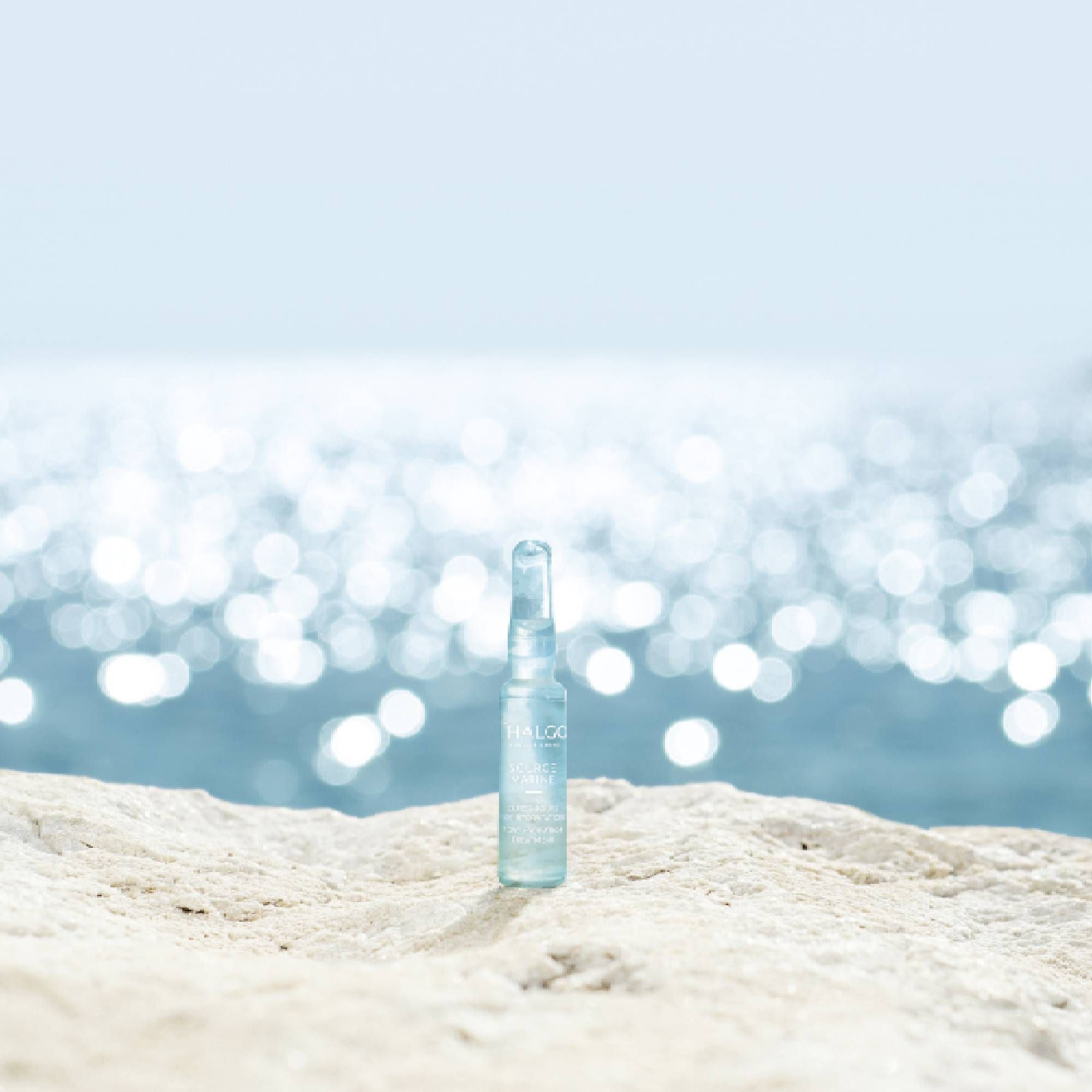 Ampulle mit bläulicher Flüssigkeit auf einem Stein vor dem Meer. Aufschrift: THALGO.