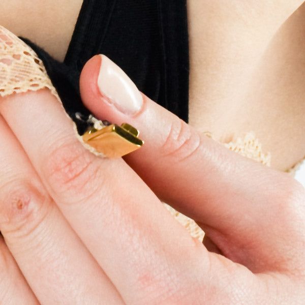 Nahaufnahme eines goldfarbenen Verschlusses an einem schwarzen BH-Träger. Finger halten den Verschluss.