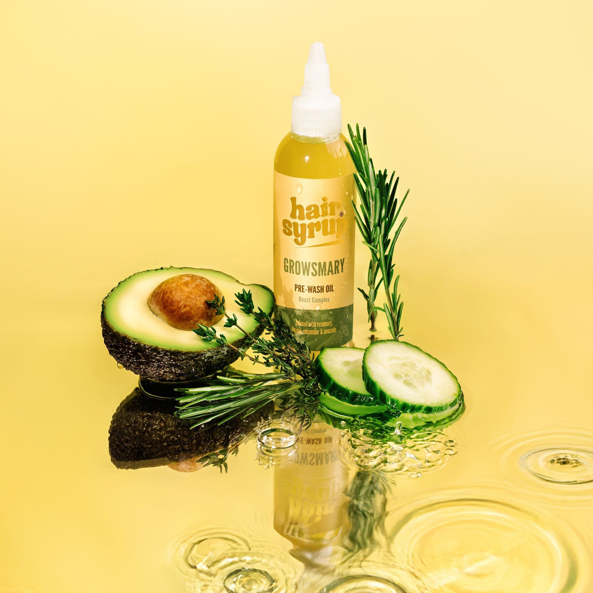 Gelbe Flasche mit „Hair Syrup Growsmary“. Daneben Avocado, Gurke, Rosmarin und Wasser. Auf gelbem Hintergrund.