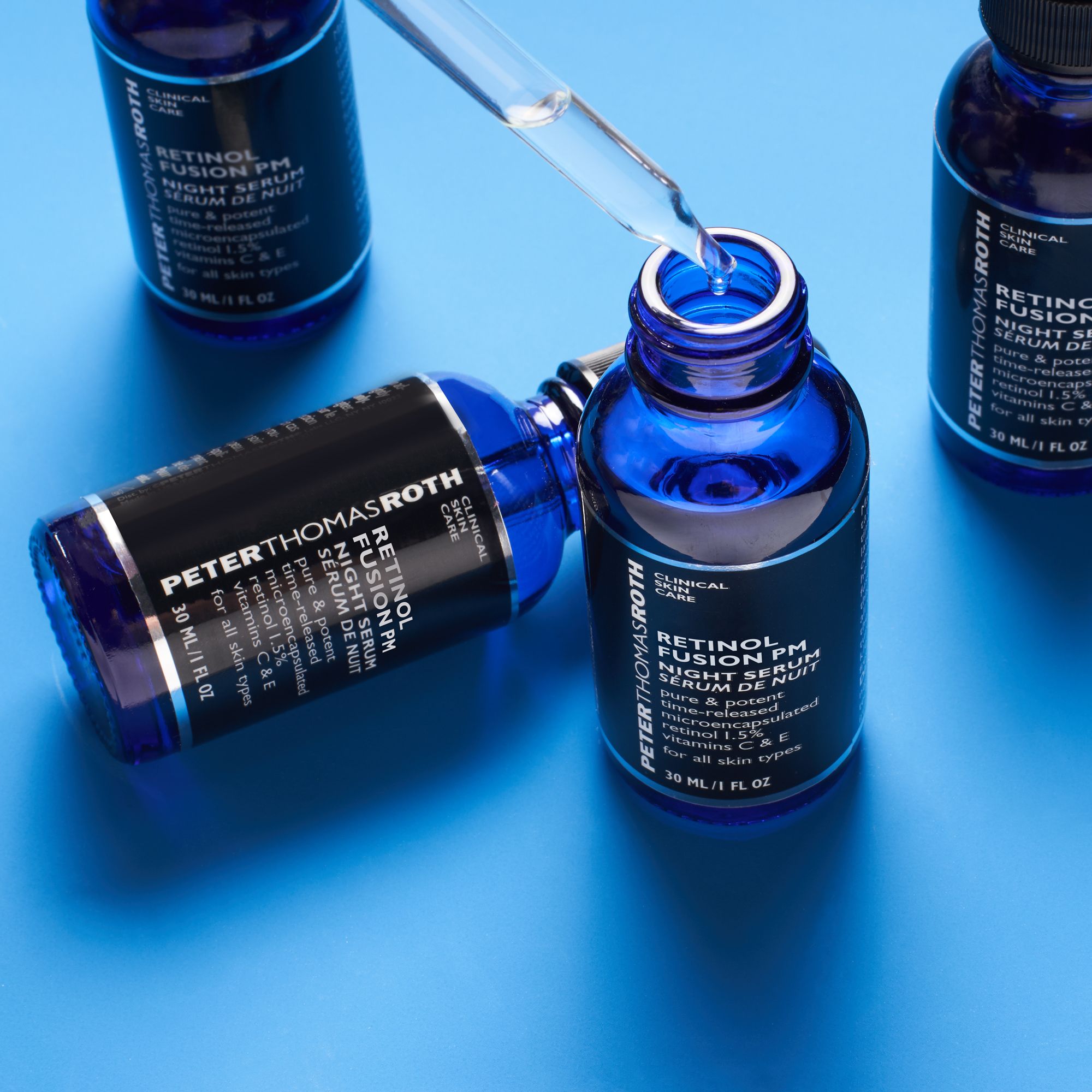 Mehrere blaue Glasflaschen mit schwarzem Deckel und Pipette auf blauem Hintergrund. Etiketten sichtbar.