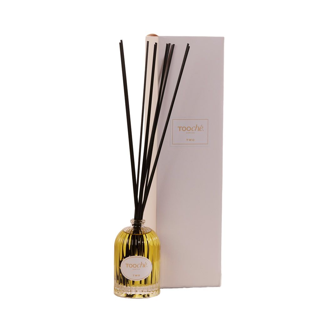 Glasflakon mit schwarzen Stäbchen und Produktverpackung. Etikett mit Schriftzug.