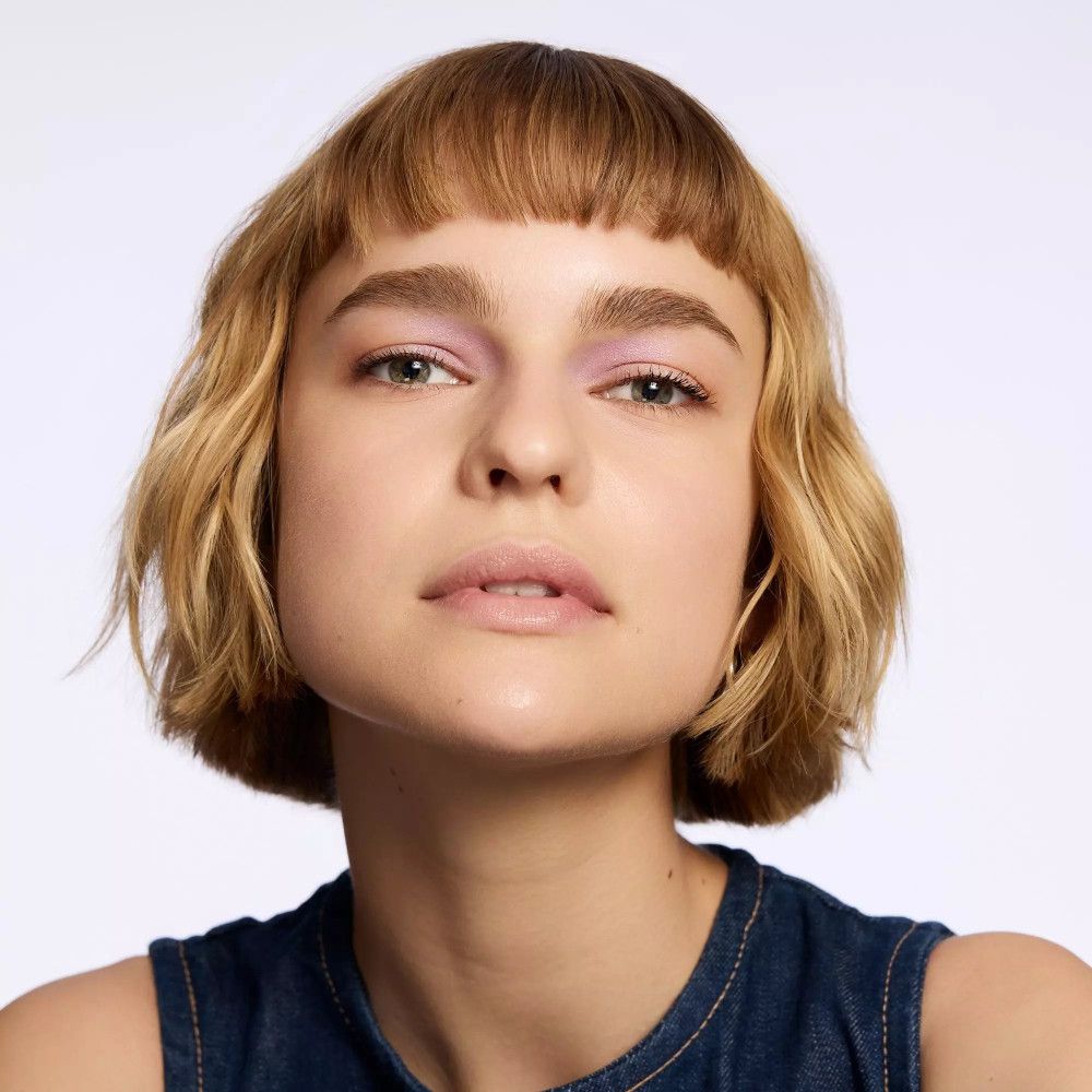 Porträt einer Frau mit blonden Haaren und lila Lidschatten. Jeanshemd.