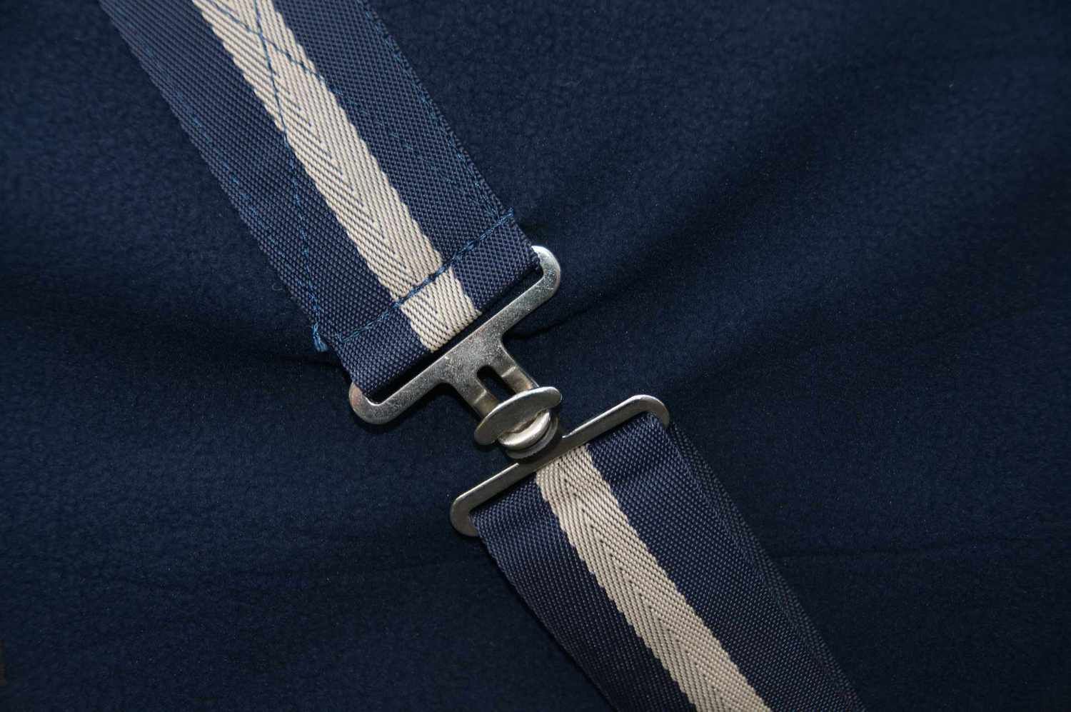 Blaues Pferdedecken-Detail mit Kreuzgurten und Metallverschluss. Beige Streifen auf den Gurten.