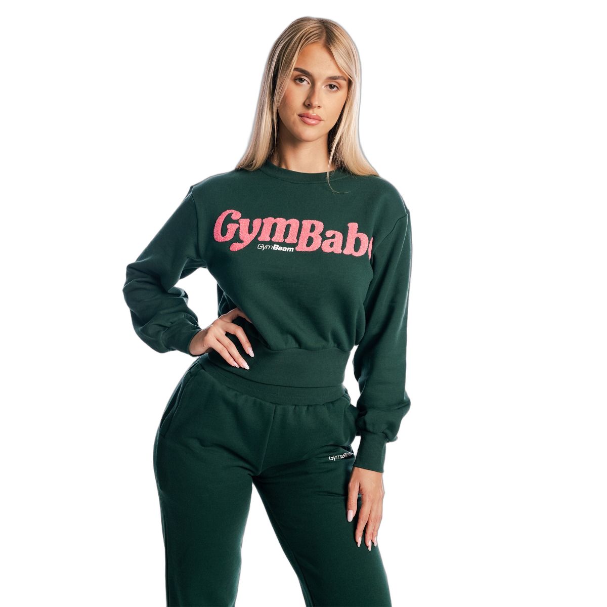 Frau im grünen Pullover cropped Langarm Forest und Jogginghose. Rosa Schriftzug 'GymBaby'.