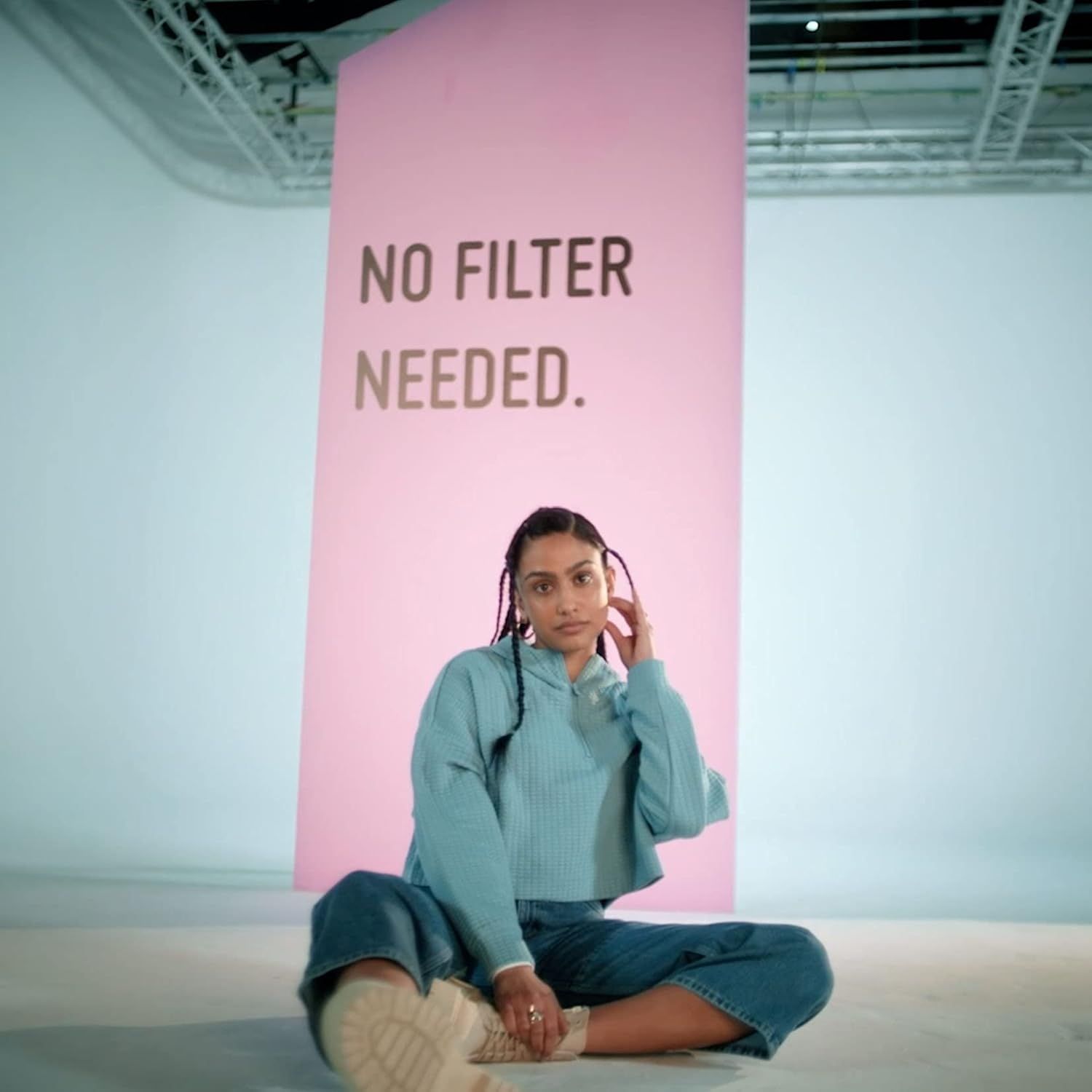 Frau sitzt vor rosa Hintergrund mit Text: NO FILTER NEEDED.