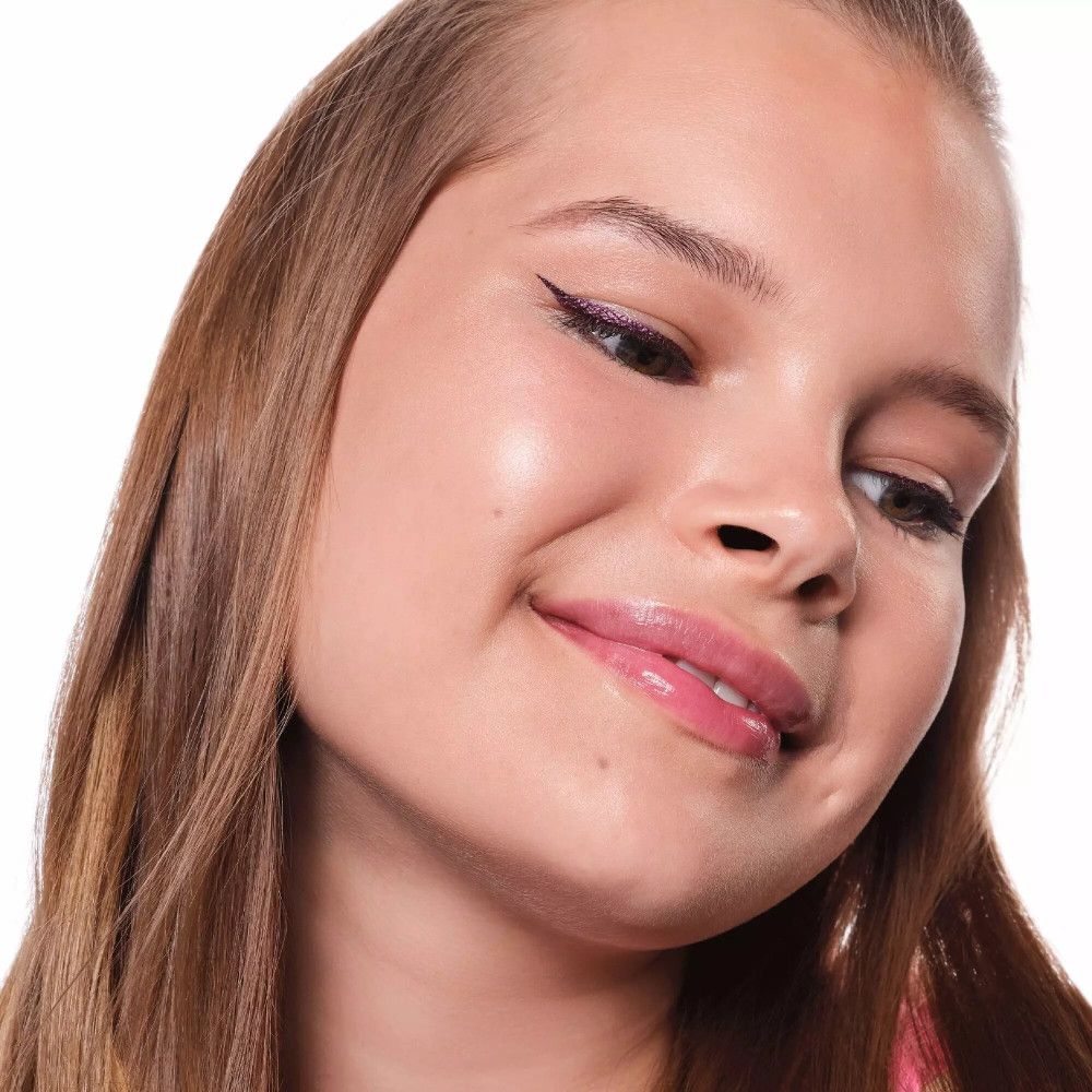 Porträt eines lächelnden Mädchens mit lila Metallic-Eyeliner. Das Mädchen hat helle Haut und trägt ein rosa Top.