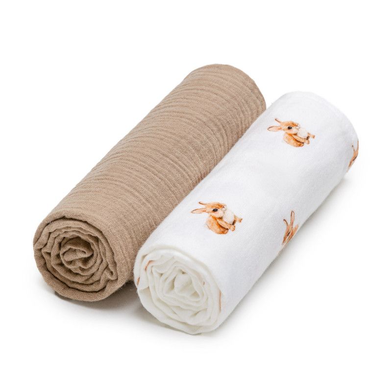 Zwei gerollte Mullwindeln. Eine beige, eine weiße mit Hasenmuster. Beide aus Stoff.