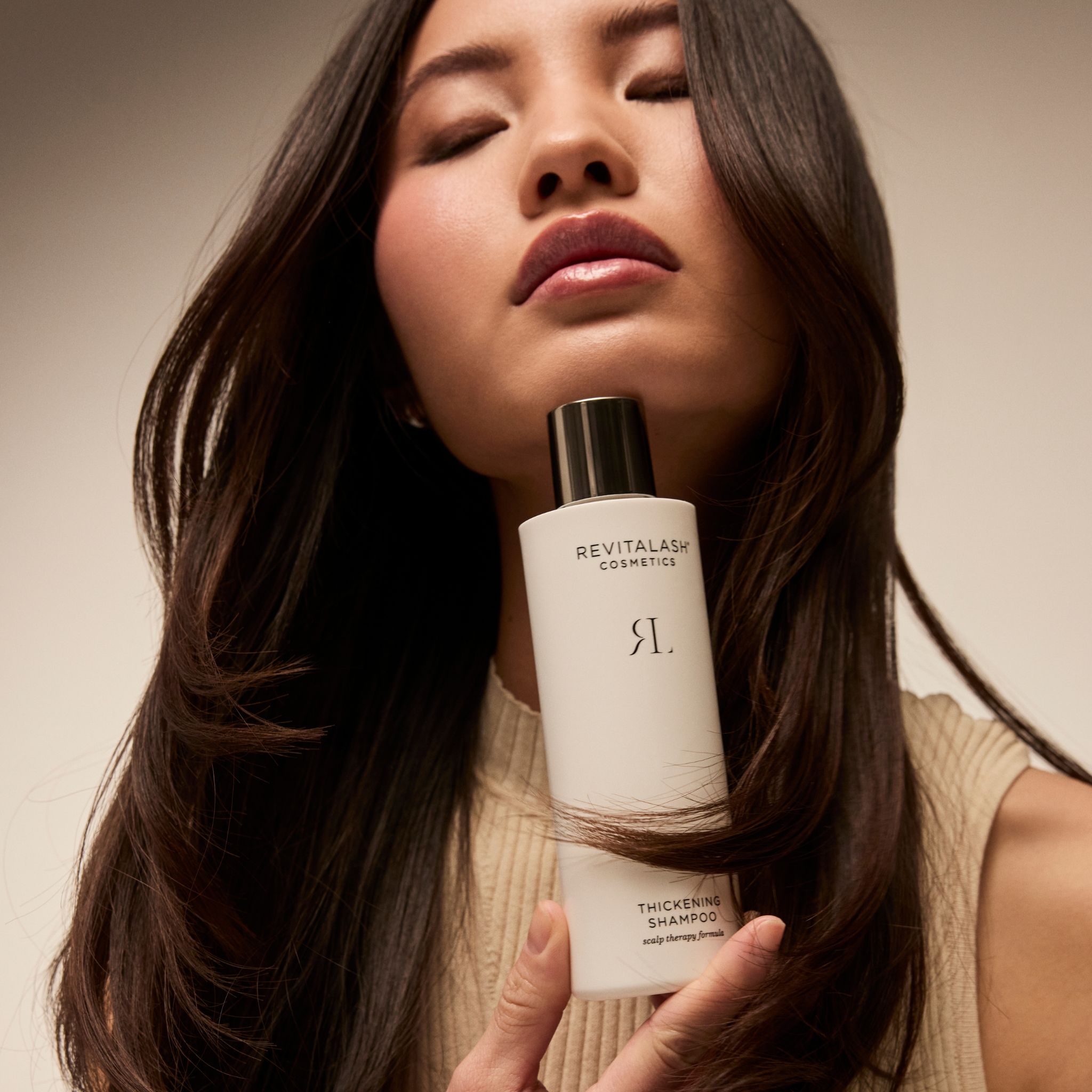 Frau hält eine Flasche RevitaLash Thickening Shampoo vor ihren langen Haaren.