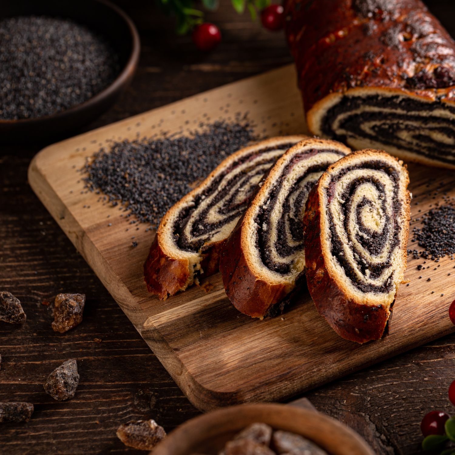 Auf einem Holzbrett geschnittenes Brot mit Mohnfüllung. Sichtbare Mohnfüllung in den Scheiben. Braune Zuckerstücke.