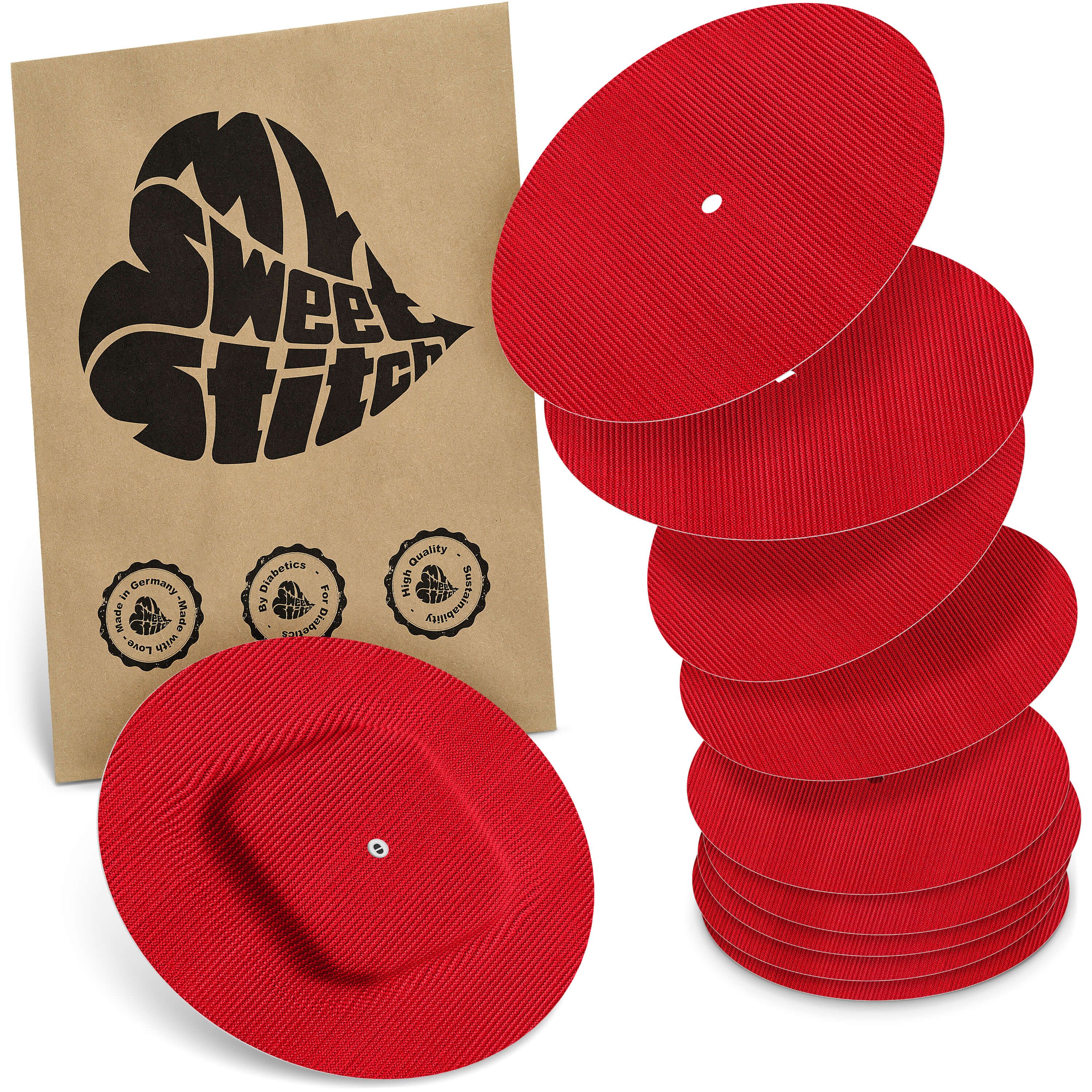 Rote, gerippte Scheiben mit zentralem Knopf, gestapelt. Eine einzelne Scheibe mit Knopf liegt vorne. Daneben eine braune Verpackung mit Herz-Logo.