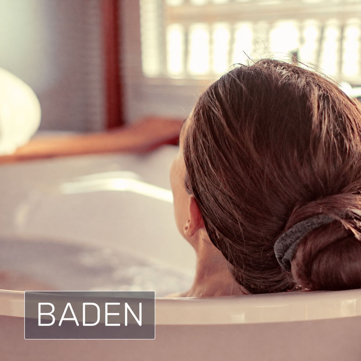 Frau in Badewanne, von hinten gesehen, mit Handtuch im Haar.