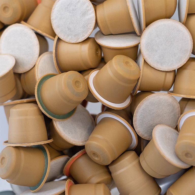 Haufen Kaffeekapseln. Braune Kapseln mit weißem Filter. Einige Kapseln sind aufgeschnitten.