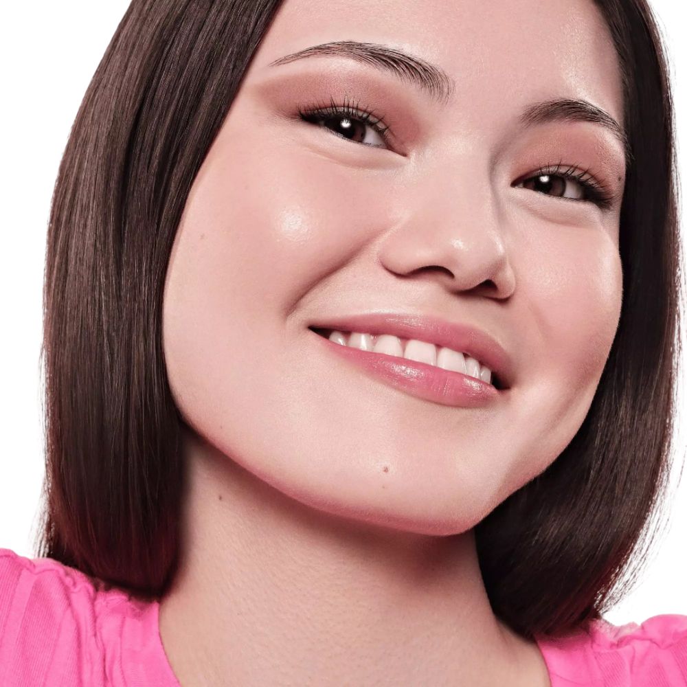 Porträt einer lächelnden Frau mit rosa Oberteil. Sie hat hellbraune Haut und Make-up.